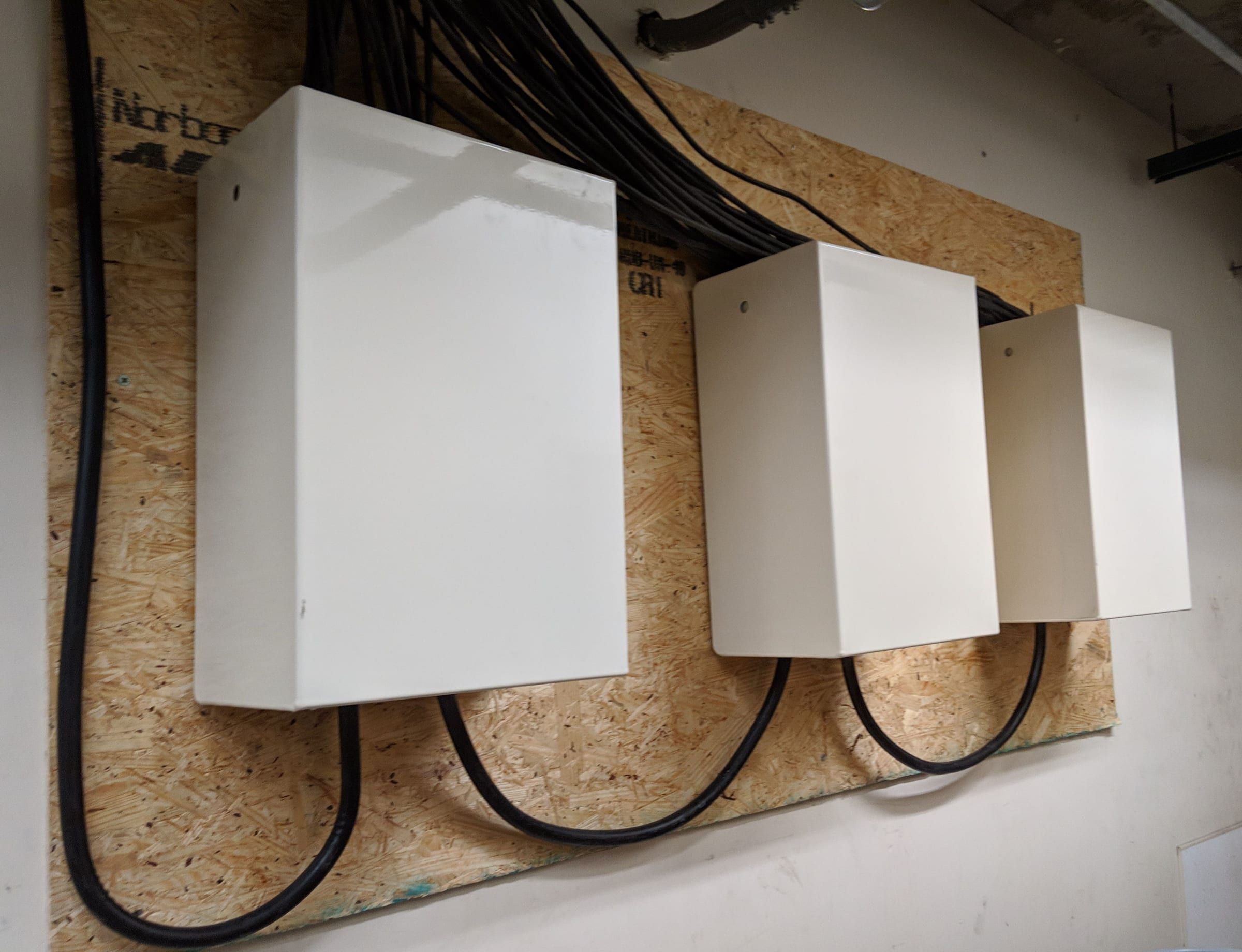 Row of three white enclosures with orderly coax loops on a plywood backboard