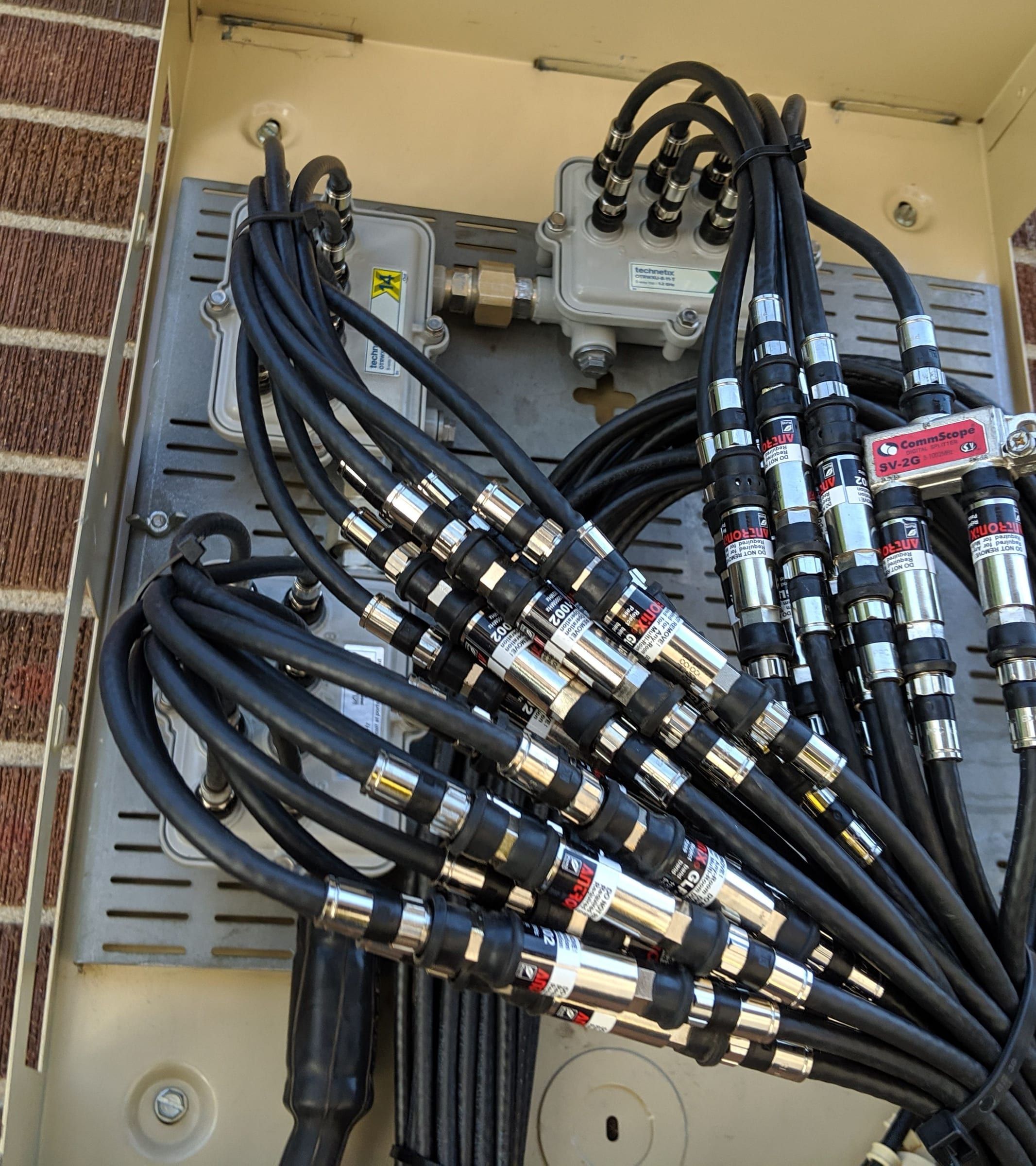 Bundle of coax drops with compression connectors landed on taps and a splitter inside a wall enclosure